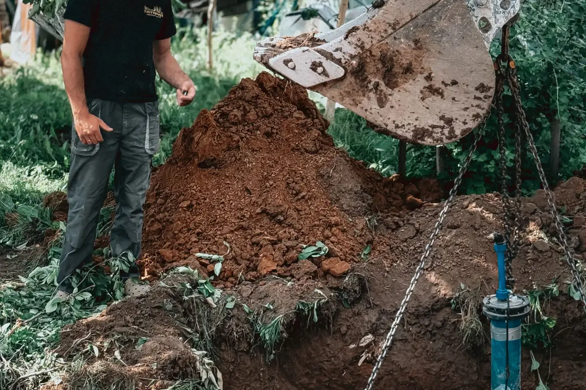 A worker beside an open excavation where a concrete chamber is being set into the ground