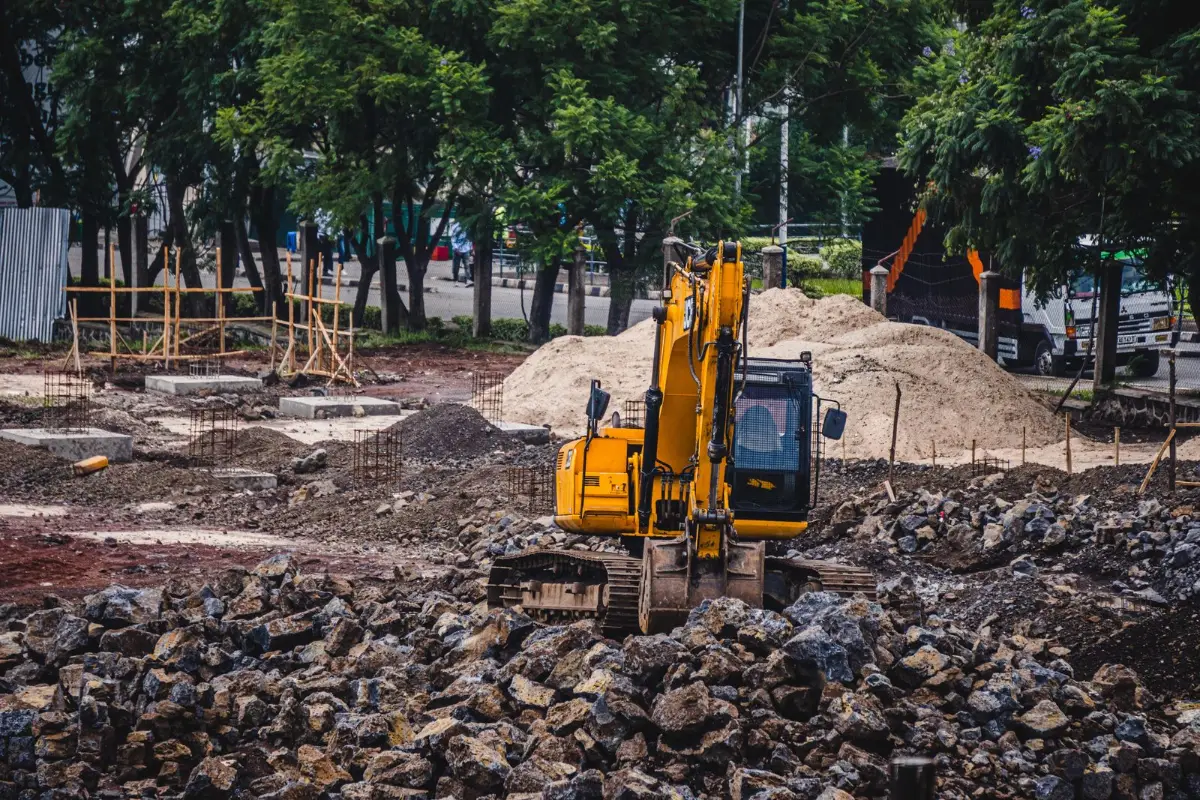 An excavator working in an open excavation beside a house lot